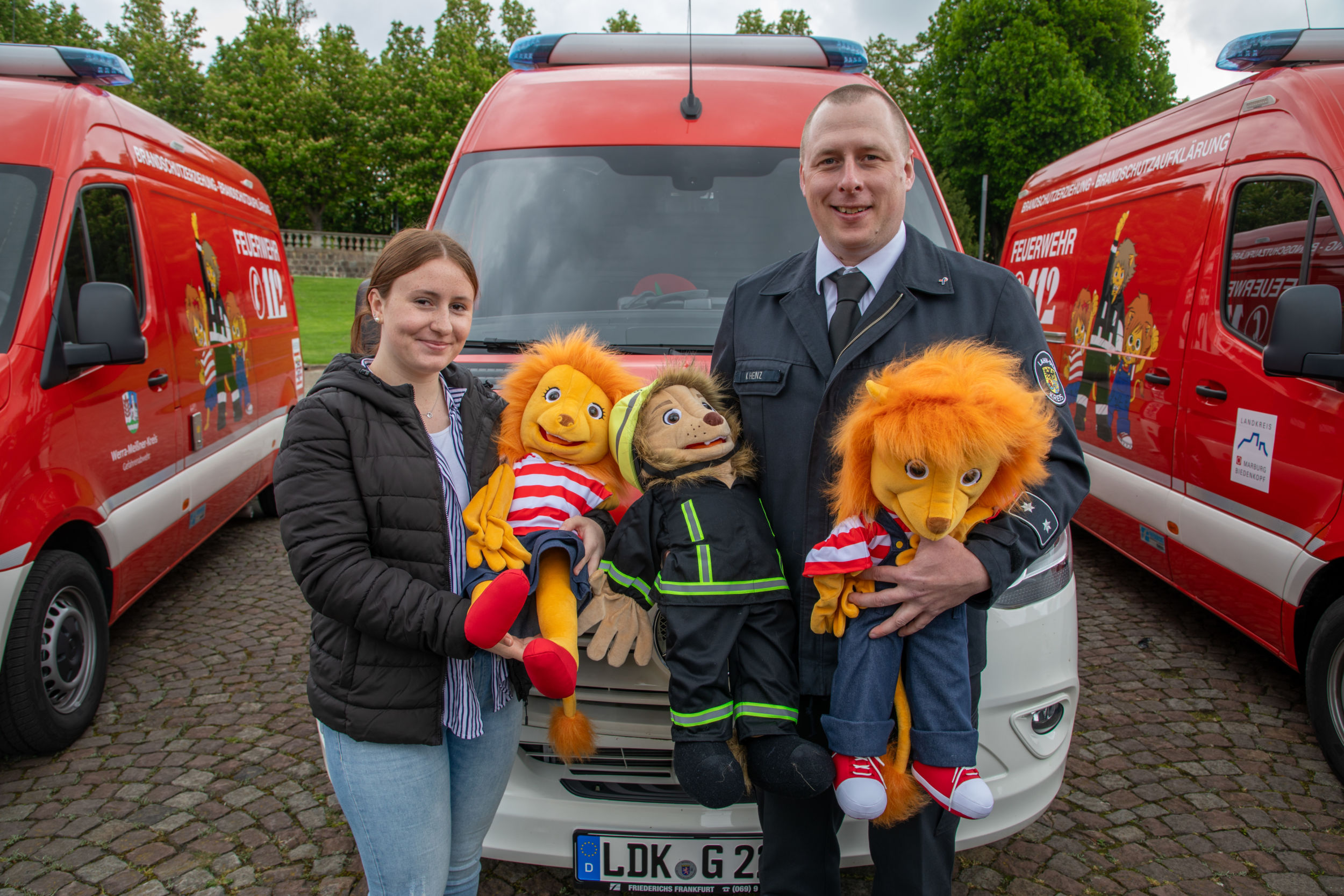 Tamina Klenz und Kristopher Heinz mit den drei Handpuppen Lenni, Leonie und Onkel Leopold vor dem neuen Gerätewagen Brandschutzerziehung. Foto: Hessisches Ministerium des Innern, für Sicherheit und Heimatschutz